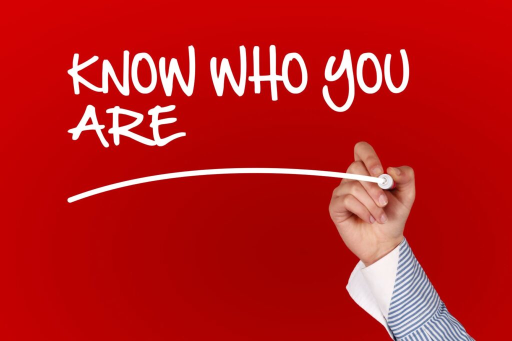 "Know Who You Are" written in white against a red background. A hand holding a white marker is underlining the words.